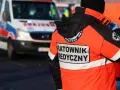 Ratownik medyczny w jaskrawej kurtce stoi obok karetki pogotowia.