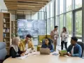 Studenci dyskutują o pedagogice przy stole, na ekranie w tle widać projekt sali lekcyjnej.