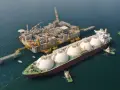 Statek LNG przycumowany do platformy wiertniczej na morzu, holowany przez holowniki.
