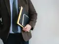 Mężczyzna w garniturze trzyma teczkę i notatnik.