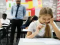 Uczennica zamyślona nad arkuszem, zastanawia się, ile trzeba mieć procent żeby zdać maturę. Nauczyciel obserwuje klasę.