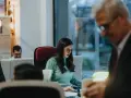 Kobieta w okularach pracuje przy biurku, obok mężczyzna w garniturze.
