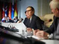 Kobieta w okularach analizuje dokumenty podczas konferencji międzynarodowej, gdzie omawiane są zagadnienia politologii.