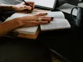 Ręce piszą w notatniku, obok otwarta księga i kubek. Studium lingwistyki stosowanej w praktyce.