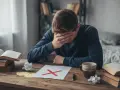 Chłopak z ręką na czole nad kartką z czerwonym krzyżykiem. Błąd kardynalny w nauce.