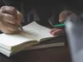 Dłoń pisze piórem w notatniku, przygotowując się do napisania rozprawki.