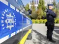 Policjant w mundurze stoi obok radiowozu. Czy zarobki w policji są adekwatne do służby?