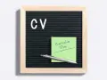 Tablica z literami "CV" i zielona karteczka z napisem "Curriculum Vitae". Idealne do przygotowania CV po niemiecku.