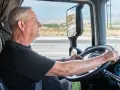Starszy mężczyzna prowadzi ciężarówkę, patrząc na drogę.