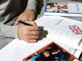 Osoba pisze długopisem w zeszycie z ćwiczeniami z języka angielskiego. Obok leży książka i flaga Wielkiej Brytanii. To pomoc w nauce, jak klauzula CV po angielsku.