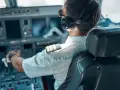 Pilot w słuchawkach i okularach przeciwsłonecznych siedzi w kokpicie samolotu, trzymając ręce na sterach.