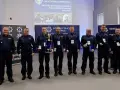 Policjanci w mundurach stoją w rzędzie, niektórzy trzymają nagrody i dyplomy.