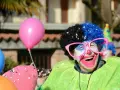 Uśmiechnięty animator w peruce i okularach, otoczony balonami, przygotowuje się do zabawy.