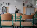 Nauczycielka przy tablicy, zastanawia się, ile zarabia przedszkolanka. Puste ławki w sali lekcyjnej.