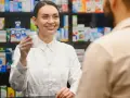 Uśmiechnięty farmaceuta podaje klientowi białe opakowanie leku.