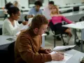 Studenci w sali wykładowej, skupieni na nauce. To dowód, że studia bez matury są możliwe i otwierają drzwi do wiedzy.