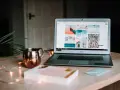 Laptop z otwartym portfolio zdjęć na ekranie, obok miedziany kubek i ozdobne lampki.