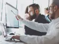 Analityk biznesowy wskazuje na wykres na monitorze, omawiając dane z kolegą.