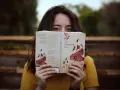 Młoda kobieta w żółtej bluzce czyta "Opowieść podręcznej" Margaret Atwood. Jej oczy błyszczą, gdy zagłębia się w świat literatury, co jest idealnym przykładem pasji do filologii.