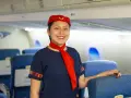Uśmiechnięta stewardessa w granatowym mundurku i czerwonym beretku stoi w samolocie, gotowa do obsługi pasażerów.