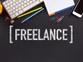 Klawiatura, telefony, ołówki i spinacze na czarnym tle. Napis "FREELANCE" sugeruje, jak zacząć pracę jako wolny strzelec.