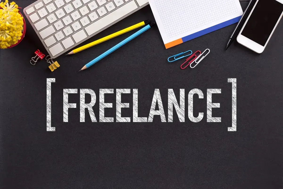 Klawiatura, telefony, ołówki i spinacze na czarnym tle. Napis "FREELANCE" sugeruje, jak zacząć pracę jako wolny strzelec.