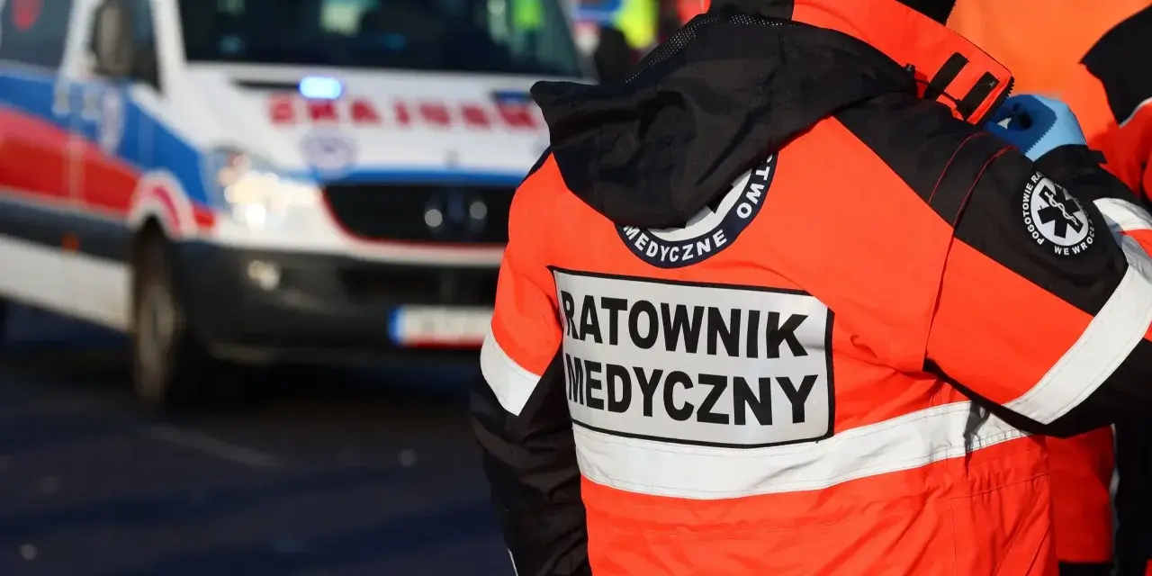 Ratownik medyczny w jaskrawej kurtce stoi obok karetki pogotowia.