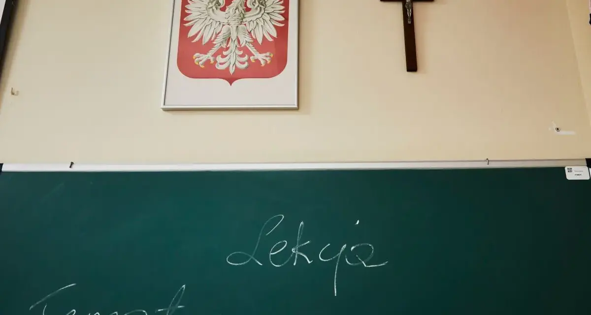 Na ścianie wisi godło Polski i krzyż. Na tablicy napisano "Temat: Lekcja". Czy religia wlicza się do średniej?