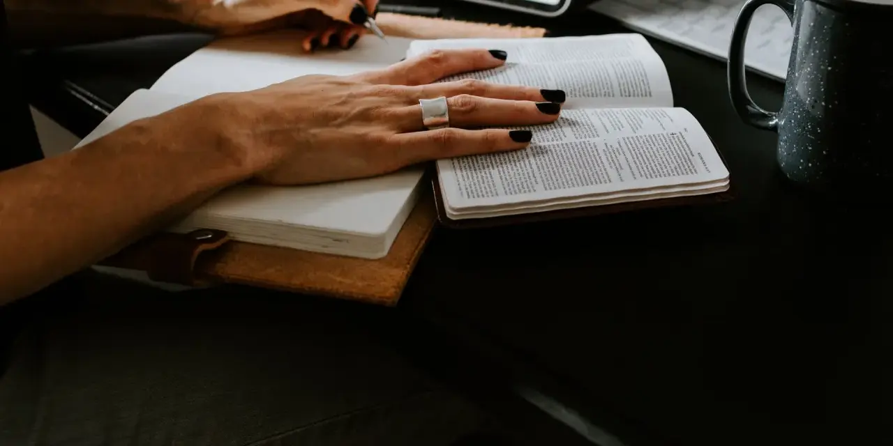 Ręce piszą w notatniku, obok otwarta księga i kubek. Studium lingwistyki stosowanej w praktyce.