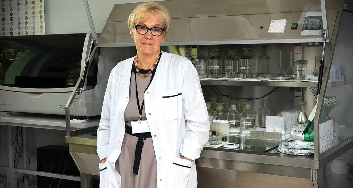 Patomorfolog w białym fartuchu stoi w laboratorium, otoczona sprzętem i odczynnikami.