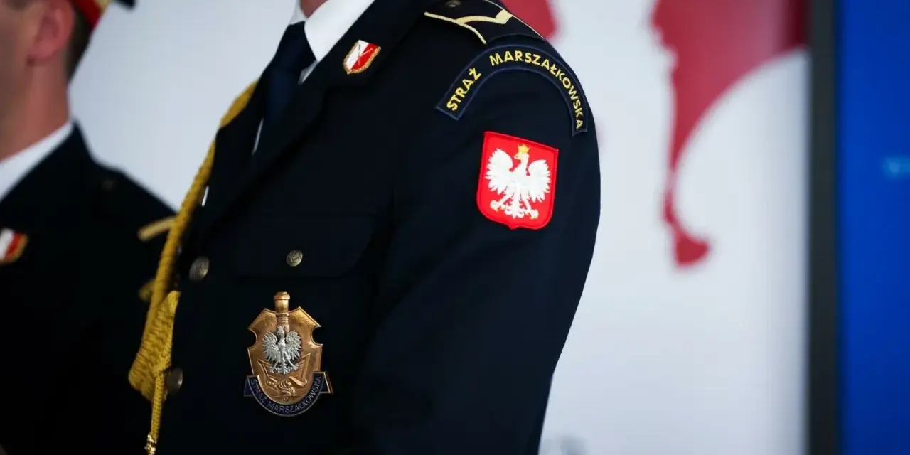 Urzędnik w granatowym mundurze z godłem Polski i napisem "STRAŻ MARSZAŁKOWSKA" na rękawie.
