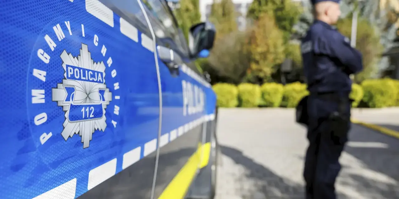 Policjant w mundurze stoi obok radiowozu. Czy zarobki w policji są adekwatne do służby?