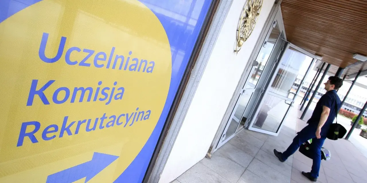 Znak "Uczelniana Komisja Rekrutacyjna" wskazuje drogę do budynku, gdzie trwa rekrutacja na studia. Mężczyzna z torbą idzie w kierunku drzwi.