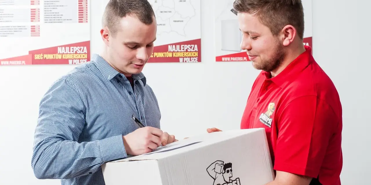 Kurier w czerwonej koszulce przekazuje paczkę, a klient podpisuje dokument. Zastanawiasz się, ile zarabia kurier?