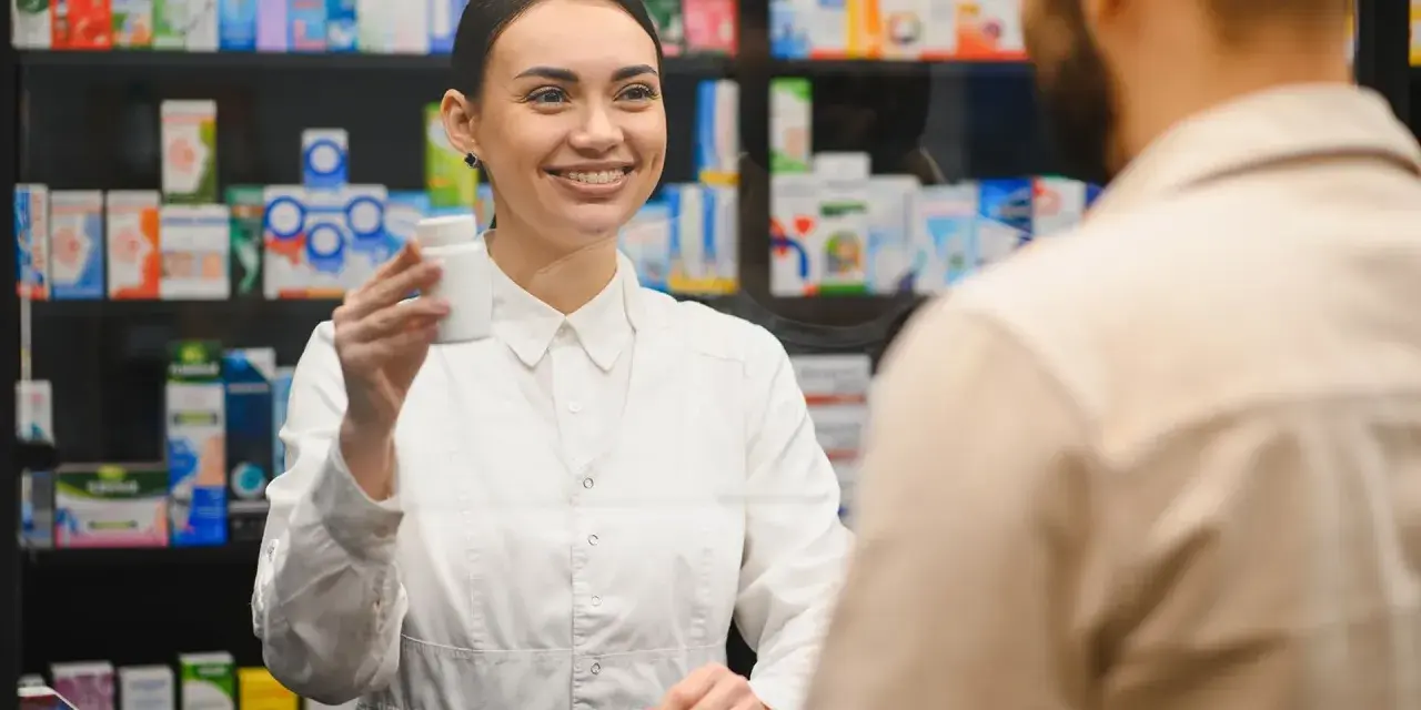Uśmiechnięty farmaceuta podaje klientowi białe opakowanie leku.