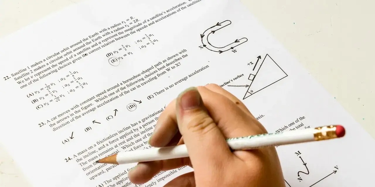 Ręka z ołówkiem rozwiązuje test fizyczny. Pytanie 22 dotyczy satelitów, a pytanie 23 ruchu po torze w kształcie podkowy. Od ilu procent jest 5?