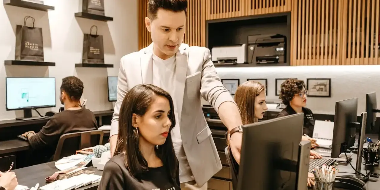 Koordynator w jasnej marynarce wskazuje coś na monitorze pracownicy.