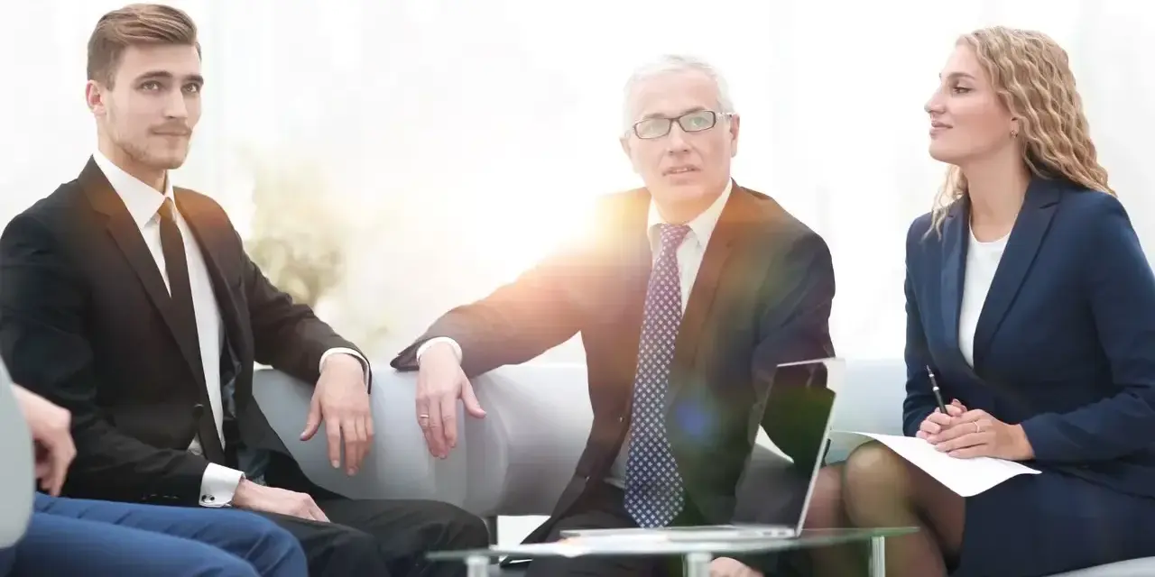 Biznesmeni dyskutują podczas spotkania. Młody mężczyzna w garniturze, starszy mężczyzna w okularach i kobieta w granatowym kostiumie tworzą zespół, który może być częścią rady nadzorczej.
