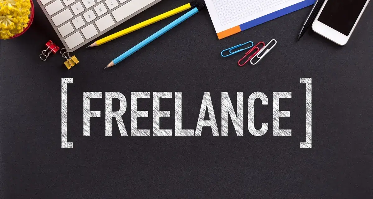 Klawiatura, telefony, ołówki i spinacze na czarnym tle. Napis "FREELANCE" sugeruje, jak zacząć pracę jako wolny strzelec.