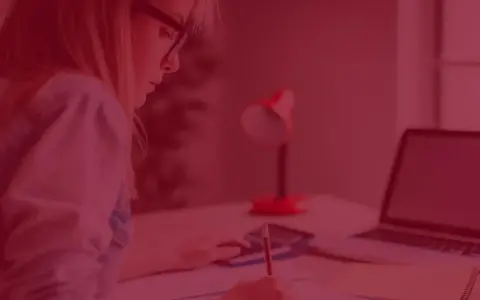 Kobieta z zeszytem i kalkulatorem zastanawia się, ile kosztują studia zaoczne. Obok leży laptop.