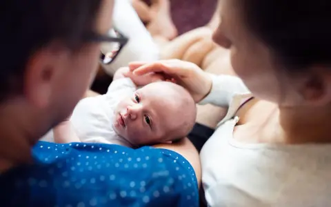 Rodzice trzymają noworodka, patrzą na niego z miłością.