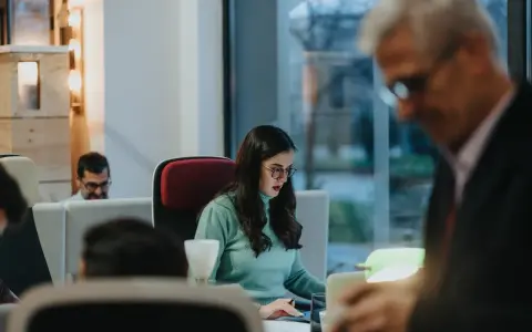 Kobieta w okularach pracuje przy biurku, obok mężczyzna w garniturze.