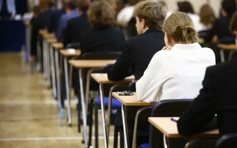 Uczniowie siedzą w rzędach przy ławkach, skupieni na rozwiązywaniu pytań maturalnych.
