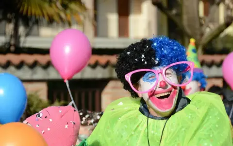 Uśmiechnięty animator w peruce i okularach, otoczony balonami, przygotowuje się do zabawy.