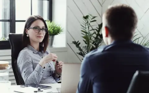 Kobieta w okularach prowadzi rozmowę kwalifikacyjną z mężczyzną.
