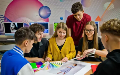 Grupa młodych ludzi dyskutuje nad próbkami kolorów i zdjęciami przy biurku.