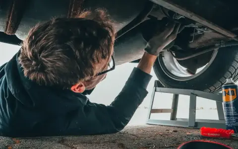 Mechanik w okularach naprawia podwozie samochodu, leżąc na ziemi.