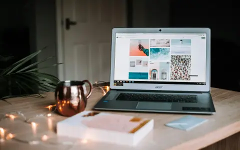 Laptop z otwartym portfolio zdjęć na ekranie, obok miedziany kubek i ozdobne lampki.