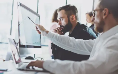 Analityk biznesowy wskazuje na wykres na monitorze, omawiając dane z kolegą.