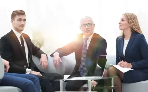 Biznesmeni dyskutują podczas spotkania. Młody mężczyzna w garniturze, starszy mężczyzna w okularach i kobieta w granatowym kostiumie tworzą zespół, który może być częścią rady nadzorczej.